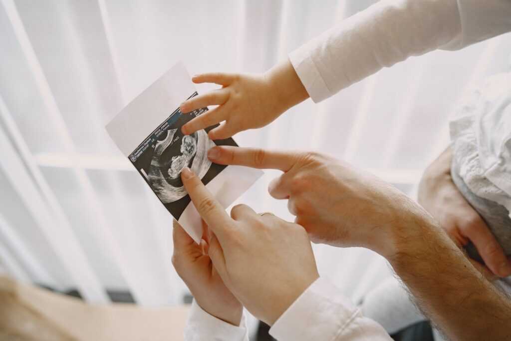mom dad daughter watching ultrasound picture baby family light clothes family expecting baby